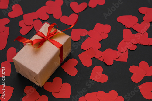 the gift box is wrapped in a red ribbon, a scroll wrapped in a red ribbon, and paper hearts around, on a black background