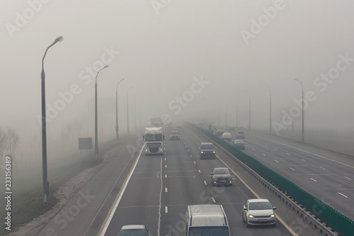 .Dense fog and poor visibility on the road. Dangerous driving situations. View on highway traffic in misty morning. Low visibility. Smoke on the road. Semi-trailer truck and cars driving trough haze © Tricky Shark