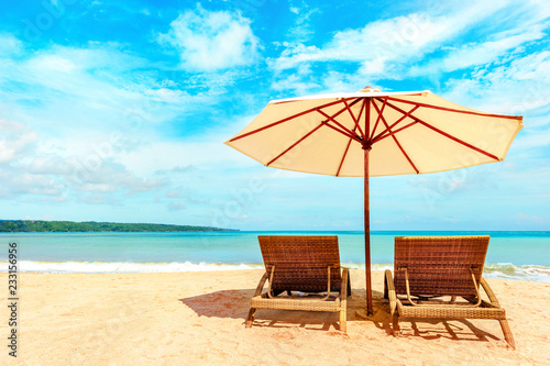Fototapeta Naklejka Na Ścianę i Meble -  Empty beach chairs and umbrella on a sandy tropical beach. Paradise Island for holidays and relaxation.