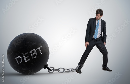 Fototapeta Young businessman has chained big metal ball to his leg with deb