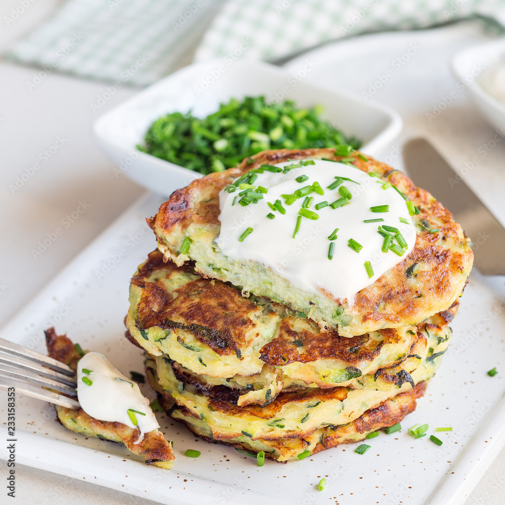 Vegetarian zucchini fritters or pancakes, served with greek yogurt and green onion on ceramic plate, square format Vegetarian zucchini fritters or pancakes, served with greek yogurt and green onion on ceramic plate, square format
