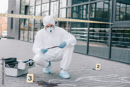 male criminologist in protective suit and latex gloves explore the murder weapon at crime scene photo