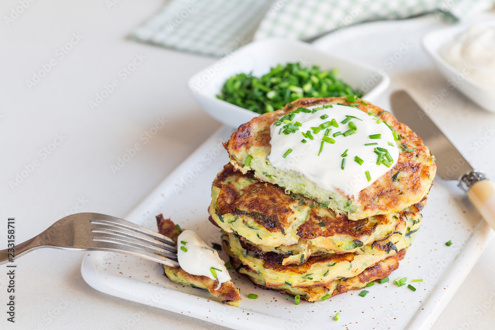 Vegetarian zucchini fritters or pancakes, served with greek yogurt and green onion on a ceramic plate, horizontal, copy space