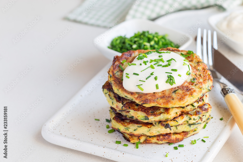 Vegetarian zucchini fritters or pancakes, served with greek yogurt and green onion on ceramic plate, horizontal, copy space