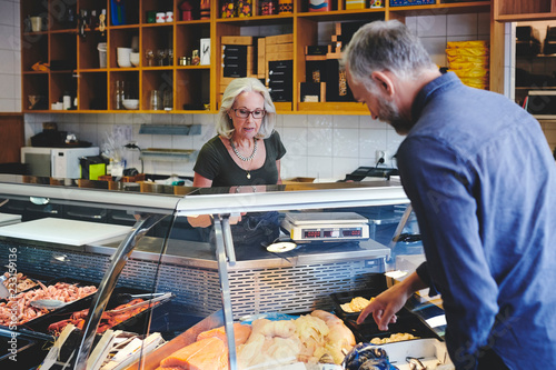Customer showing seafood at retail display to saleswoman in deli photo