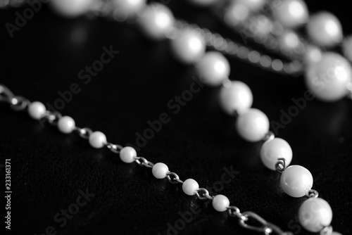 Necklace of white beads and metal chain on a dark background close up. Black and white