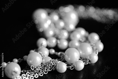 Necklace of white beads and metal chain on a dark background close up. Black and white