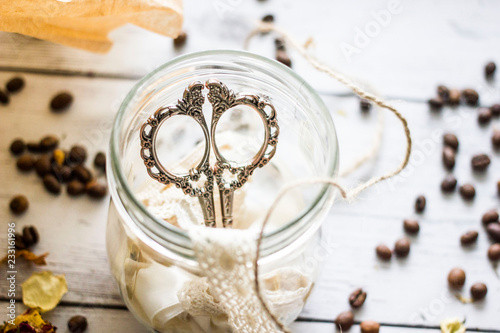 Vintage and handmade background. Decorative scissors for sewing on a glass jar with lace and braid on a wooden background