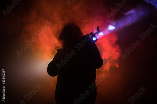 Silhouette of man with assault rifle ready to attack on dark toned foggy background or dangerous bandit in black wearing balaclava and holding gun in hand. Shooting terrorist with weapon theme decor