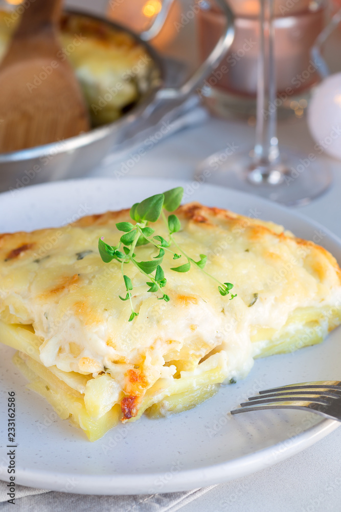 Piece of cheesy scalloped potatoes or potato gratin on plate, holiday theme, vertical Piece of cheesy scalloped potatoes or potato gratin on plate, holiday theme, vertical