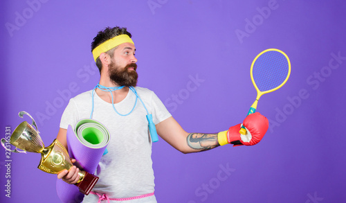 Sport shop assortment. Choose favorite sport. Sport concept. On way to achievement. Man bearded athlete hold sport equipment jump rope fitness mat boxing glove expander racket and golden goblet © be free