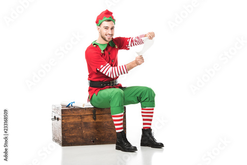 Cuadro en lienzo cheerful man in christmas elf costume sitting on wooden chest and holding wishli