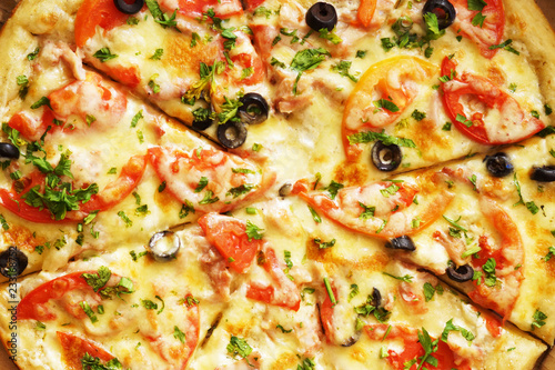 Hot pizza with cheese, ham and chicken, fresh tomato slices and olives cutted to pieces, top view. Could be used as food background or in restaurant menu 