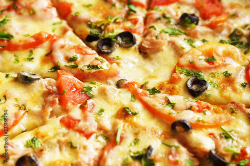 Hot pizza with cheese, ham and chicken, fresh tomato slices and olives cutted to pieces, side view. Could be used as food background or in restaurant menu