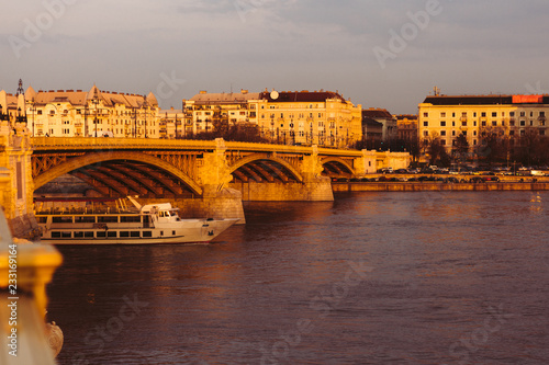 The touristic ship sails on the Danube under the Margaret Bridge in Budapest during the orange sunset - golden hour 