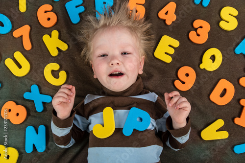 Happy charming Caucasian blond's kid in colored clothes playing with plastic letters. Learning the alphabet, preparing for school. Education for kindergarten and preschool children. Black background