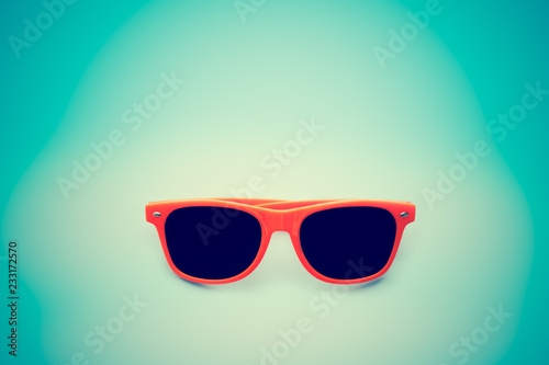 Summer orange sunglasses isolated in vignetting blue background. Minimal concept image for sun protection, hot days, tropical travel, summer vacation holidays. Photo toned for retro vintage look.