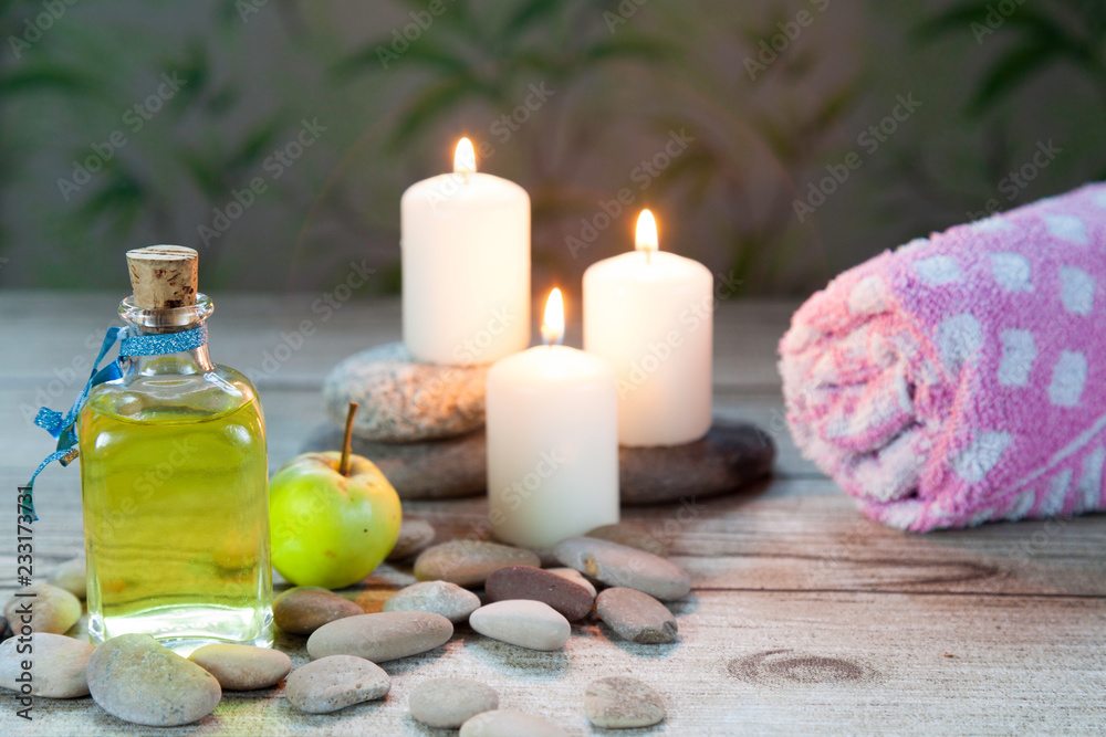 bottle of  oil massage, river pebbles and a small green apple