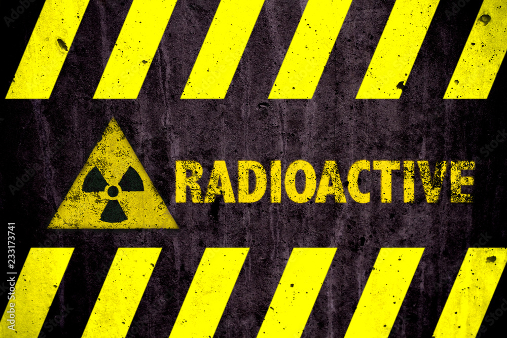 Radioactive (ionizing radiation or nuclear energy) danger symbol and word with yellow and hazard black stripes painted on a massive concrete wall with rustic texture background.