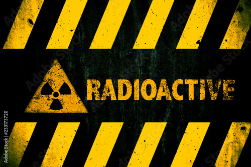 Radioactive (ionizing radiation or nuclear energy) danger symbol and word with yellow and hazard black stripes painted on a massive concrete wall with dark rustic texture background with vignetting.