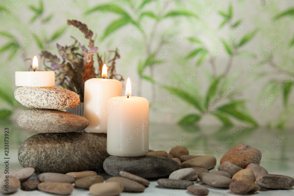 Three lighted candles on river pebbles with lavender on herbal background