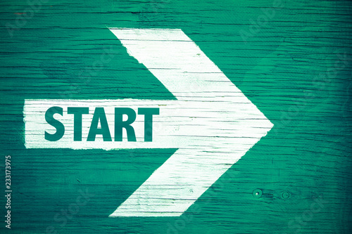 Start text written on white directional arrow pointing right painted on a green wooden signboard background. Motivation concept for start line for business begin and professional career path. photo