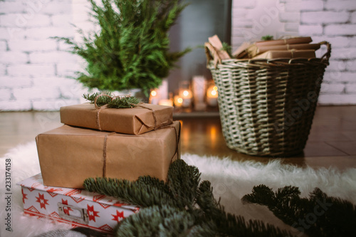 Christmas gifts on the background of the Christmas tree, fireplace decorated with burning candles and wicker basket with gifts. The concept of a winter holiday.