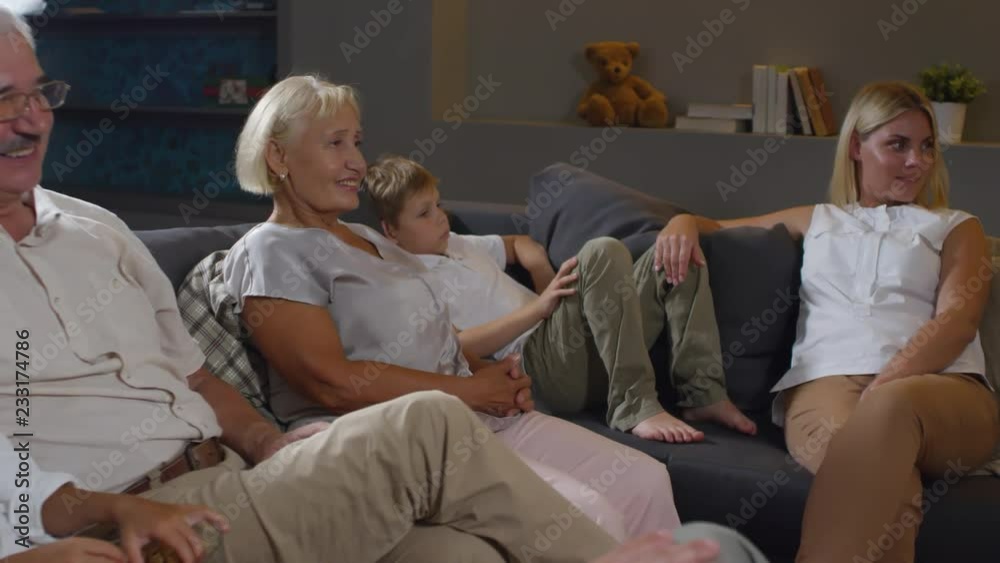 Mother, father, grandparents and little boy and girl sitting together on comfortable sofa in the living room, speaking and watching TV together Mother, father, grandparents and little boy and girl sitting together on comfortable sofa in the living room, speaking and watching TV together