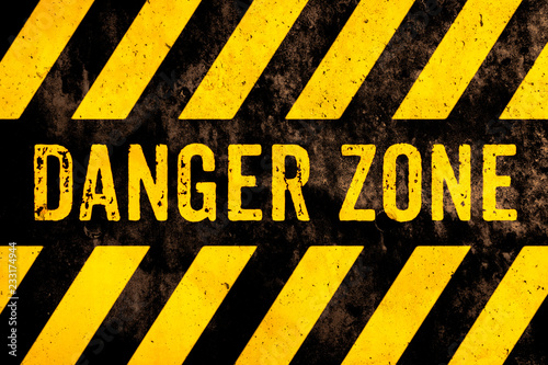 Danger zone warning sign text with yellow and black stripes painted over concrete wall surface facade cement texture background. Concept image for caution, risky dangerous area and hazard. photo