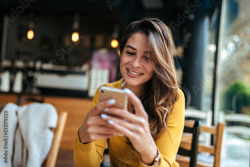 Beautiful young woman reading text message on mobile phone at the cafe.