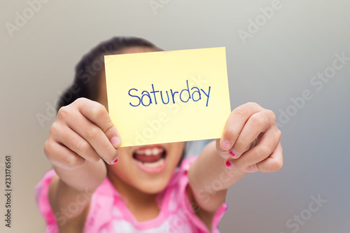 little girl show yellow note with saturday word