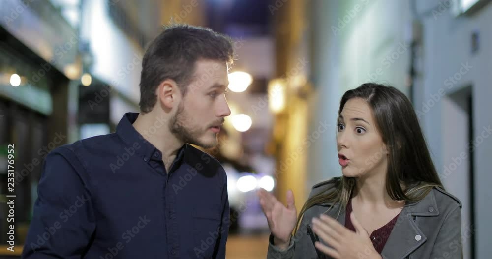 Front view of an angry couple arguing in the night walking towards camera in the street Front view of an angry couple arguing in the night walking towards camera in the street