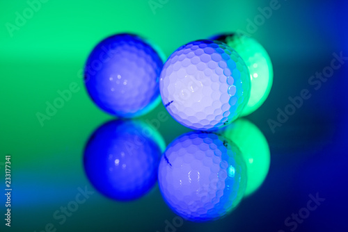White golf balls mirroring on glass illuminated in green and blue