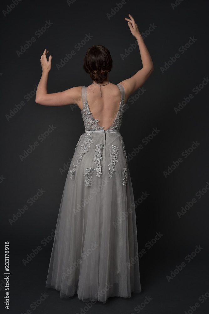 full length portrait of brunette girl wearing beautiful long gown, standing pose with background to the camera on grey studio background. full length portrait of brunette girl wearing beautiful long gown, standing pose with background to the camera on grey studio background.