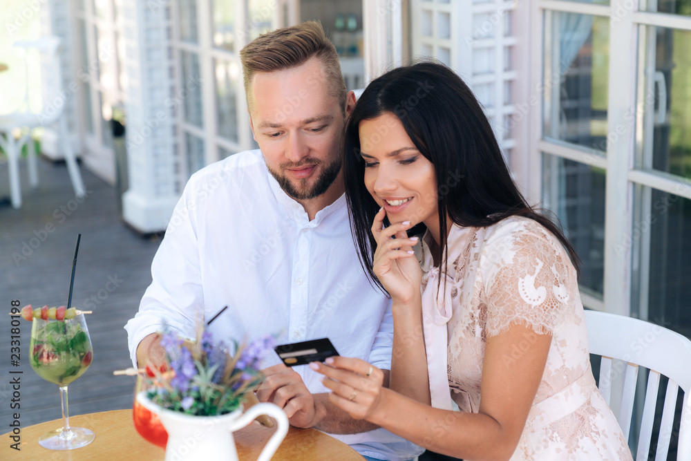 A close-up of a man and a woman paying an account in a cafe using a bank credit card. The girl holds a plastic card, wants to pay the bill for cocktails and desserts. Concept people, internet A close-up of a man and a woman paying an account in a cafe using a bank credit card. The girl holds a plastic card, wants to pay the bill for cocktails and desserts. Concept people, internet