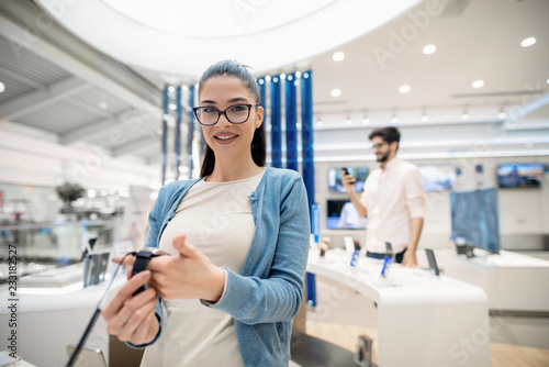 Woman holding in hands smart watch while standing in tech store and looking in camera.
