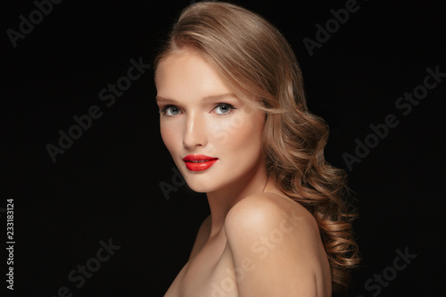 Portrait of young gorgeous woman with wavy hair and red lipstick dreamily looking in camera over black background isolated