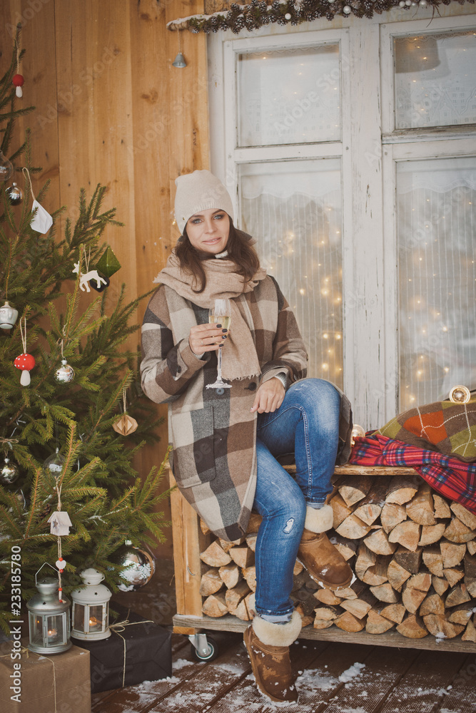 Girl celebrates Christmas outdoors. Christmas terrace with a decorated Christmas tree and snow and garland lights. A gift in hand.
