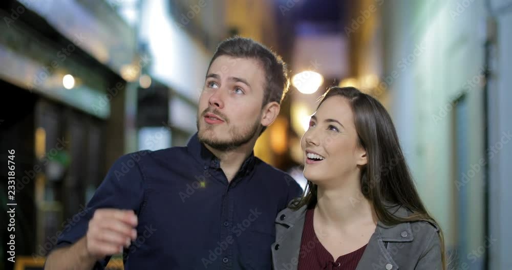 Front view of a happy couple walking towards camera sightseeing in the night in the street Front view of a happy couple walking towards camera sightseeing in the night in the street