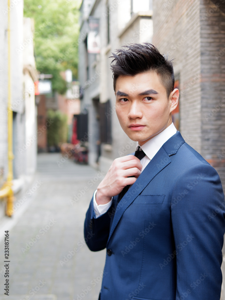 Portrait of a handsome businessman adjusting tie, close up upper body view. Attractive male hipster Chinese model. Portrait of a handsome businessman adjusting tie, close up upper body view. Attractive male hipster Chinese model.