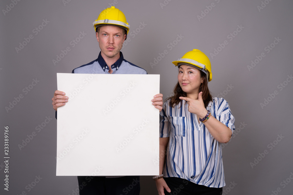 Businessman and mature Asian businesswoman wearing hardhat Businessman and mature Asian businesswoman wearing hardhat
