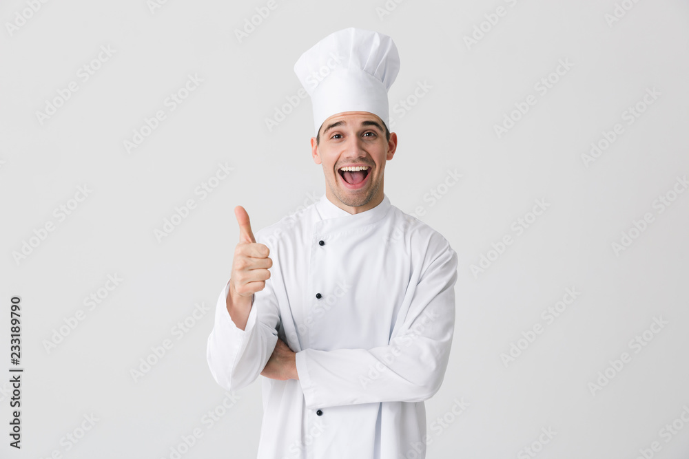 Excited young man chef indoors isolated over white wall background showing thumbs up gesture. Excited young man chef indoors isolated over white wall background showing thumbs up gesture.