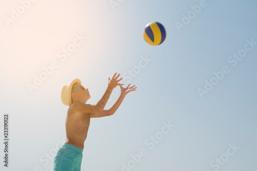 Kid play volleyball on sea beach, against sunny sky background