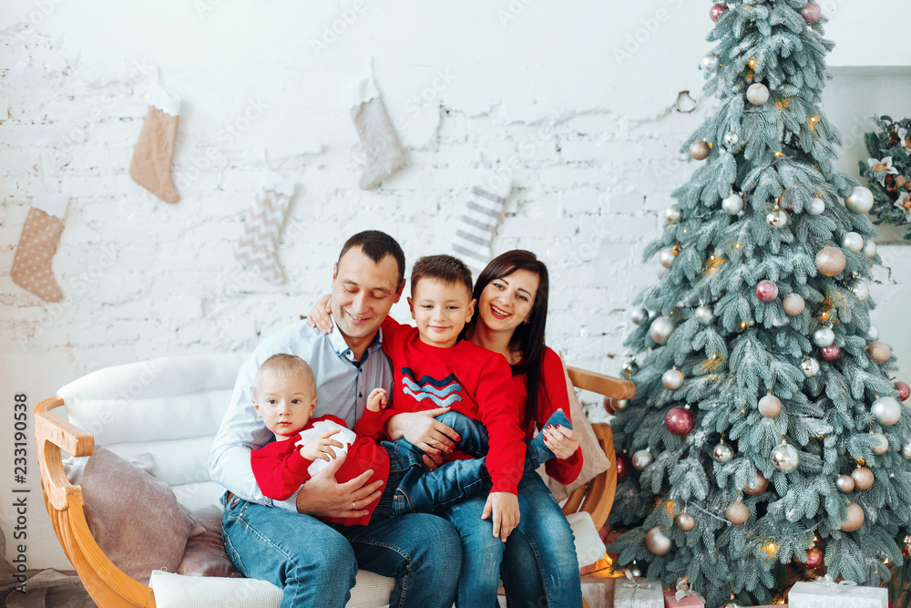 Happy Young Family With Two Children Holding Christmas Gift and Smiling at Camera Near Christmas tree. New Year Celebration. Decorations.  Xmas event