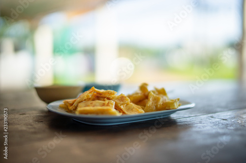 Yellow egg roti in blue plastic pot on wooden table with blurred background.