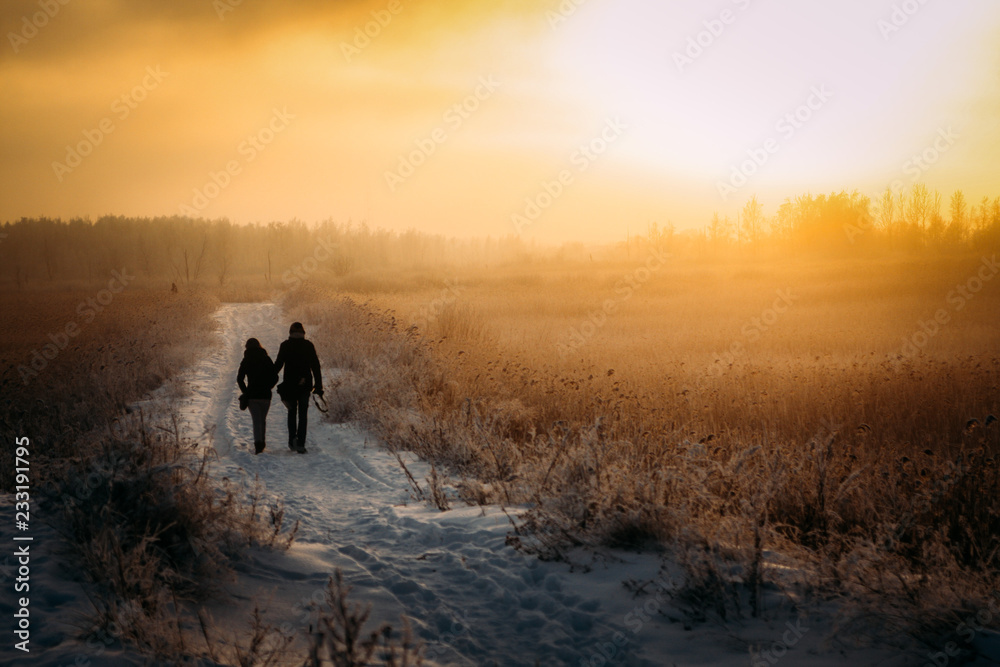silhouette of a couple walking in the snowy road on sunset silhouette of a couple walking in the snowy road on sunset