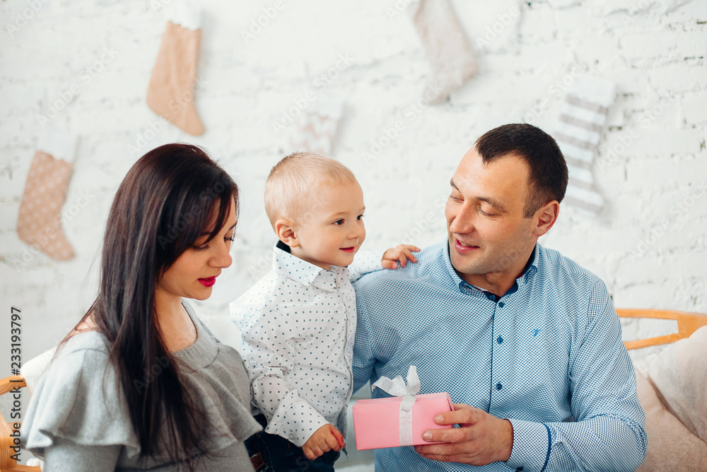 Happy Young Family With Two Children Holding Christmas Gift and Smiling at Camera Near Christmas tree. New Year Celebration. Decorations.  Xmas event