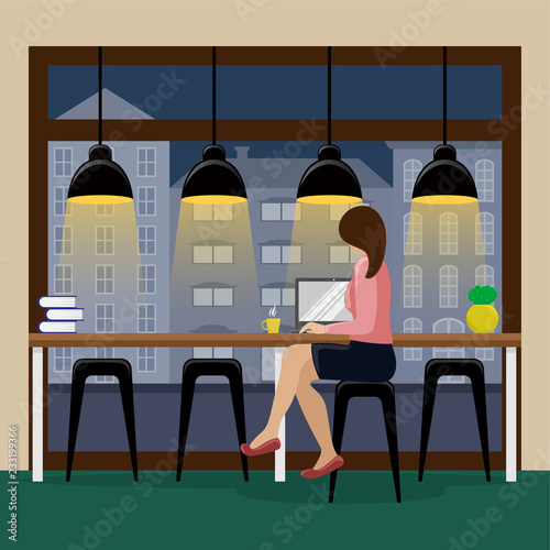 Woman working at the computer at the bar counter near the panoramic window in the coffee house. City view. Place to work.