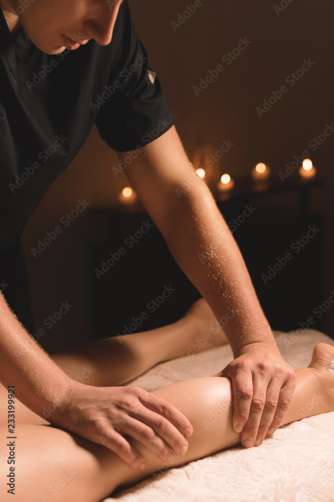 Obraz premium Close-up of male hands doing calf massage of female legs in a dark room with candles in the background. Cosmetology and spa treatments