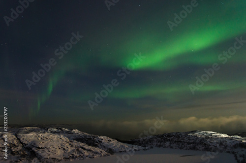 Beautiful northern lights, aurora in the night sky over the snow-covered hills.